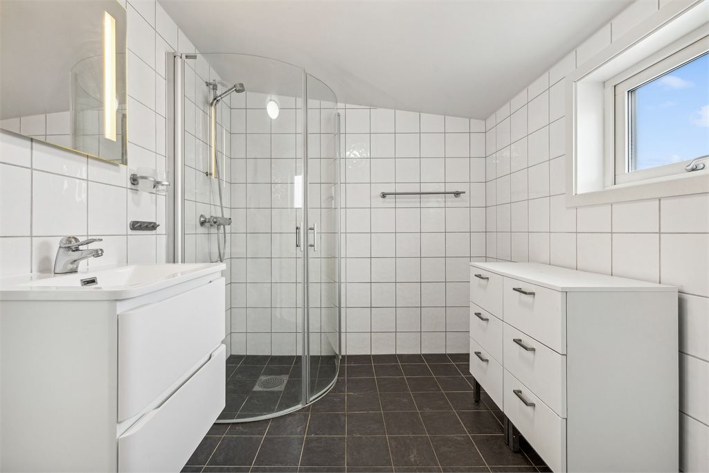 Badet er innredet med vegghengt toalett, vask i seksjon, speil med belysning og dusjhjørne.