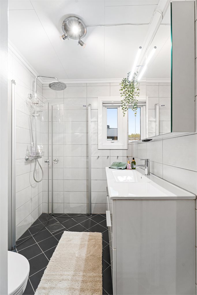 Badet i denne etasjen er helfliset i tidløse fliser med dusjhjørne, vegghengt toalett og flott innredning med speil og oppbevaring. 
