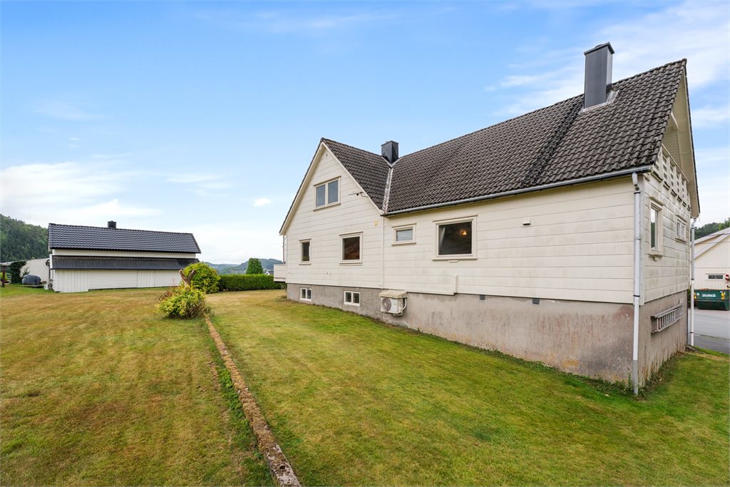 Boligen sett fra hagen – romslig tomt med plen og frittstående uthus/garasje.